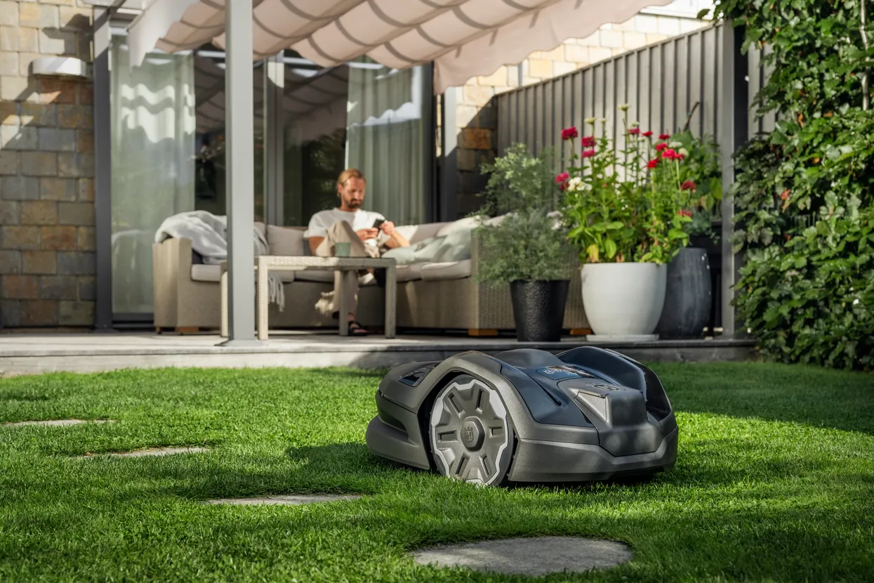 Husqvarna Automower® 305E NERA. Robotic lawn mower operating on a well-maintained lawn in a garden setting.