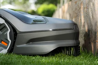 Husqvarna Automower® 305E NERA. Robotic lawn mower operating close to a garden wall.