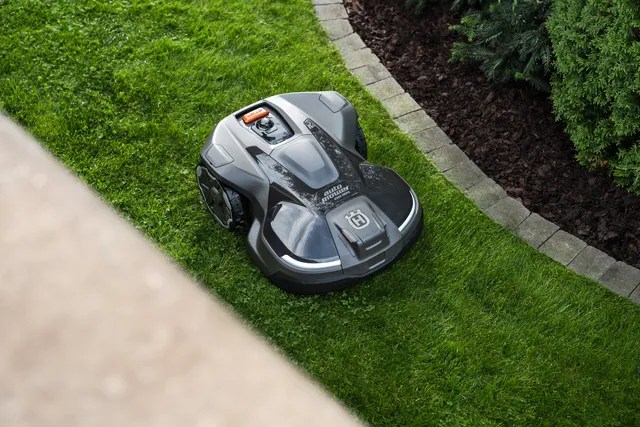 Robotic lawn mower operating on a neatly trimmed lawn near a stone border.
