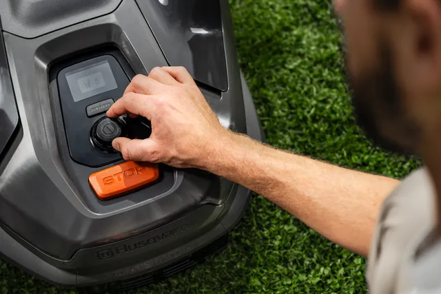 A person adjusting the settings on a Husqvarna robotic lawn mower in a garden.